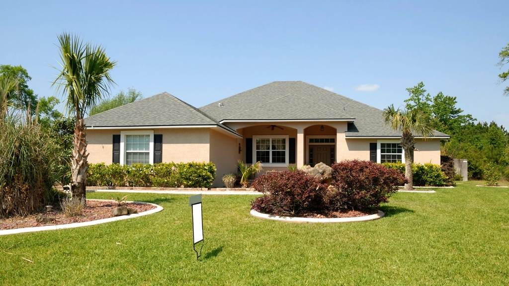 Single-story Florida home with a green lawn, palms and planted beds